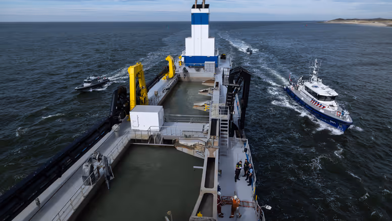 Een politieboot en een rhib-boot van de Koninklijke Marechaussee flankeren een groot schip.