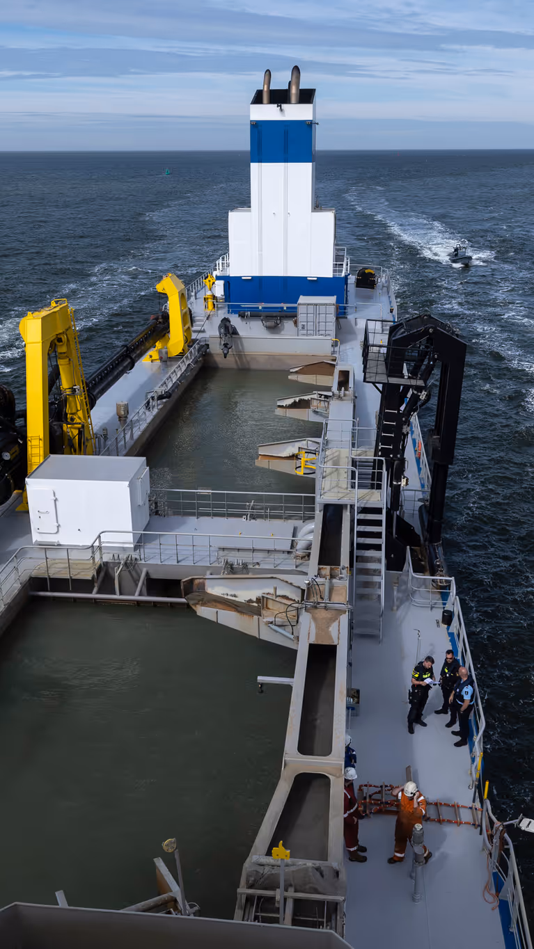 Een politieboot en een rhib-boot van de Koninklijke Marechaussee flankeren een groot schip.