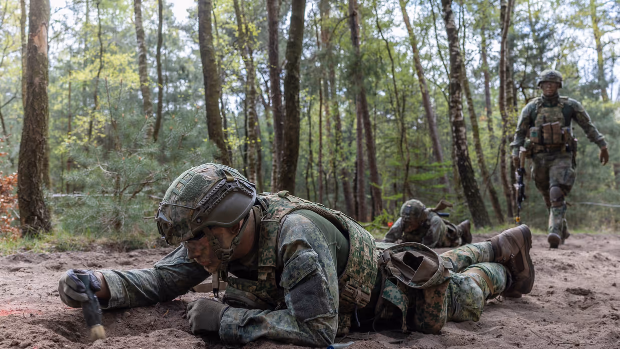 Militairen liggen op hun buik en vegen een mijn af.