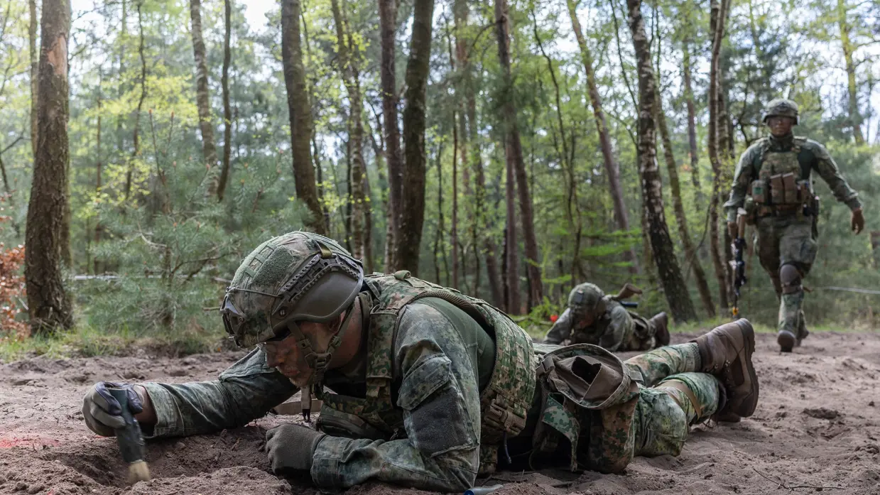 Militairen liggen op hun buik en vegen een mijn af.
