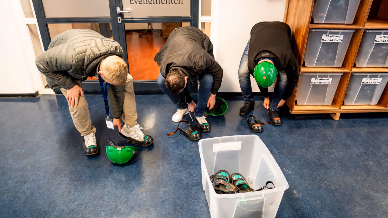 Drie mannen bukken om veiligheidsschoenen aan te trekken.