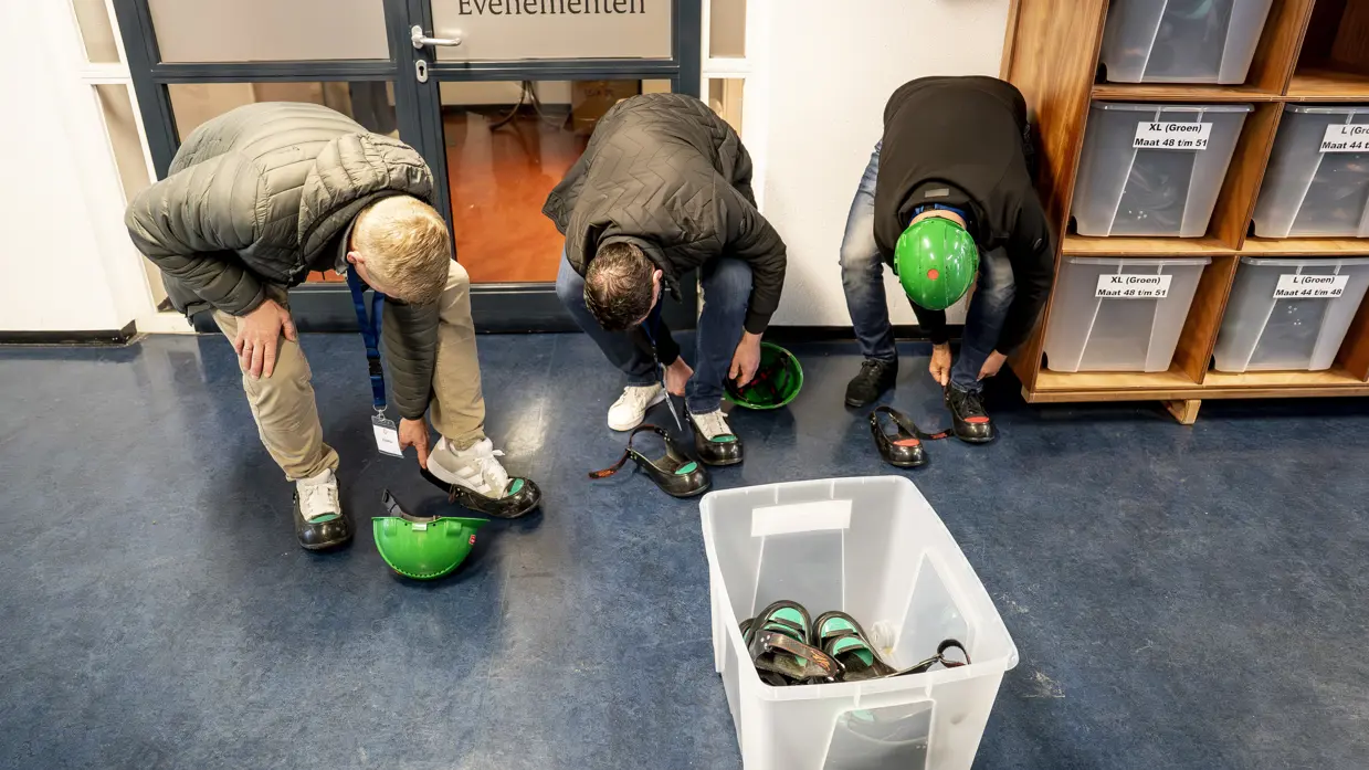 Drie mannen bukken om veiligheidsschoenen aan te trekken.