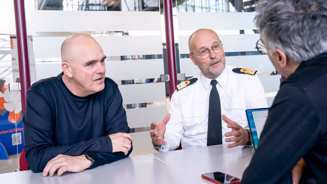 Militair en burgermedewerker aan tafel in gesprek met interviewer.