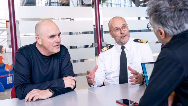 Militair en burgermedewerker aan tafel in gesprek met interviewer.