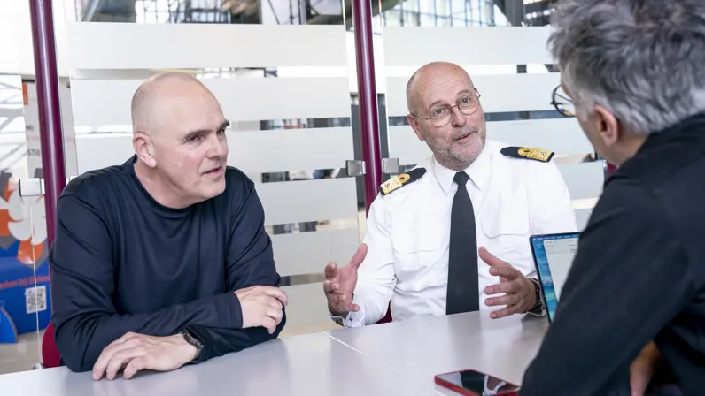 Militair en burgermedewerker aan tafel in gesprek met interviewer.