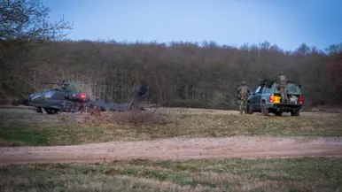 Een militaire helikopter staat stil in een veld, terwijl twee soldaten bij een groene terreinwagen met open laadbak staan. Rechts: het interieur van een helikopter tijdens zonsondergang. Twee piloten zitten in de cockpit, omlijst door oranje en donkere kleuren aan de lucht. 