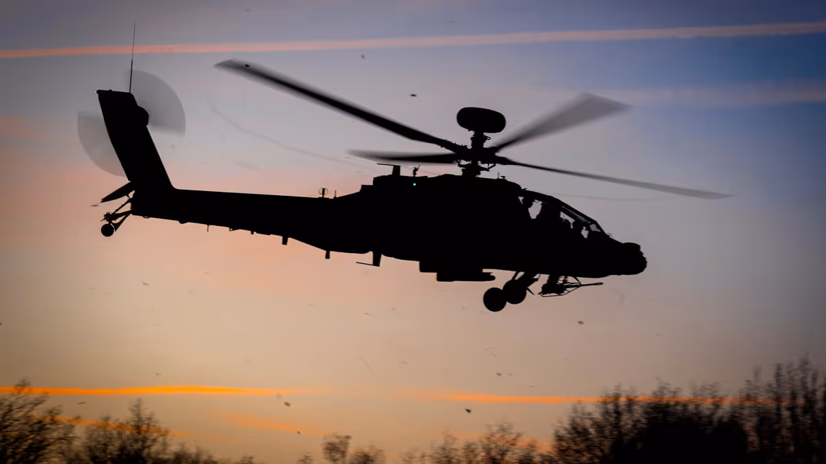 Een Apache-helikopter vliegt in de lucht met schemerend zonlicht in de achtergrond.
