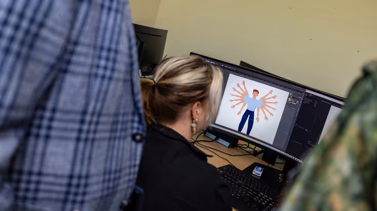 Een jonge vrouw kijkt naar een computerscherm. Op het scherm is een marechausseepoppetje te zien met zijn armen in verschillende posities.