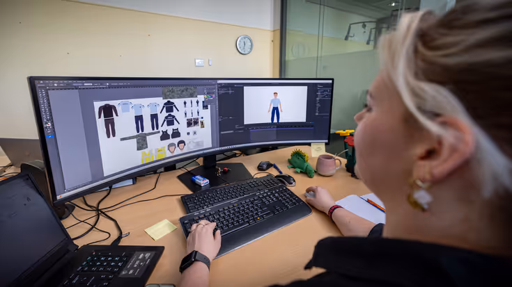 Een jonge vrouw kijkt naar een breed, holvormig computerscherm. Op het scherm is een animatie te zien van een marechausseepoppetje en verschillende soorten kleding. 