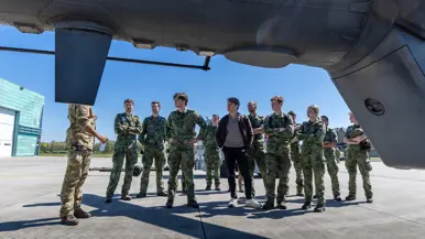 Jonge militairen en een burger krijgen uitleg van een militair   naast een helikopter. 