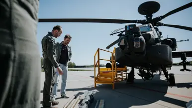  Boswijk krijgt uitleg van een militair over de verschillende soorten munitie en bewapening die uitgestald op de grond liggen voor een Apache.
