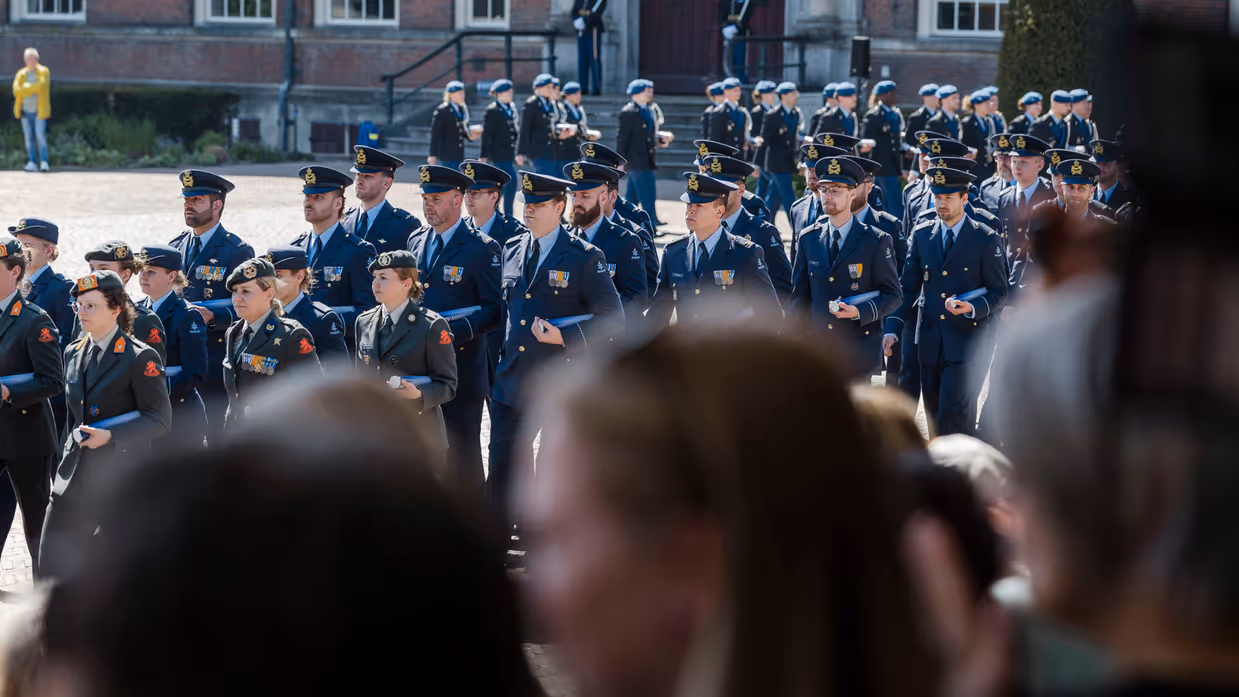 Over de schouders van het publiek zie je de cadetten van de verschillende krijgsmachtsdelen de Parade van de KMA op marcheren.