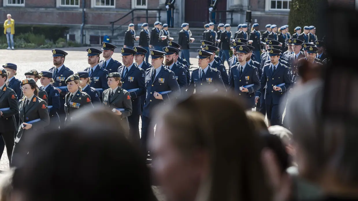 Over de schouders van het publiek zie je de cadetten van de verschillende krijgsmachtsdelen de Parade van de KMA op marcheren.