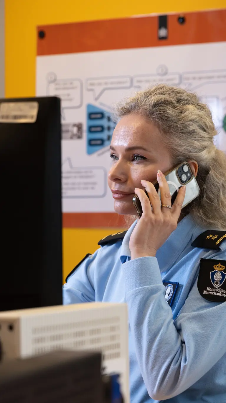 Luitenant-kolonel Irena zit achter een computer en houdt een telefoon bij haar oor.
