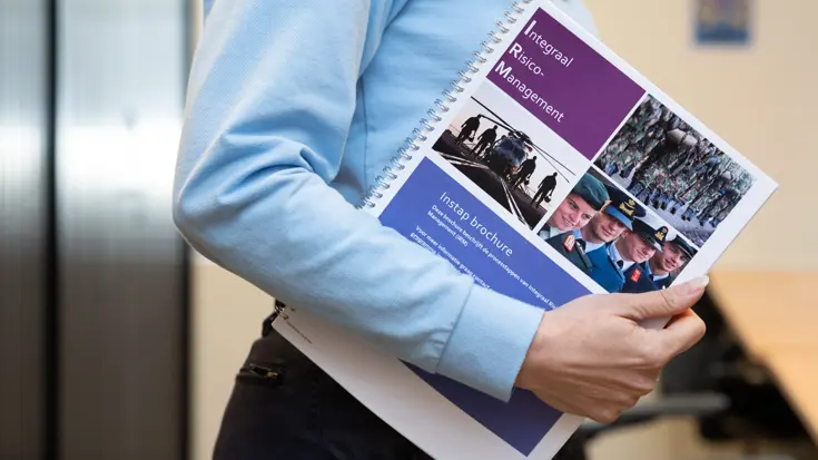 Irena van de zijkant gezien, terwijl ze een folder over Integraal Risicomanagement vasthoudt onder haar arm.
