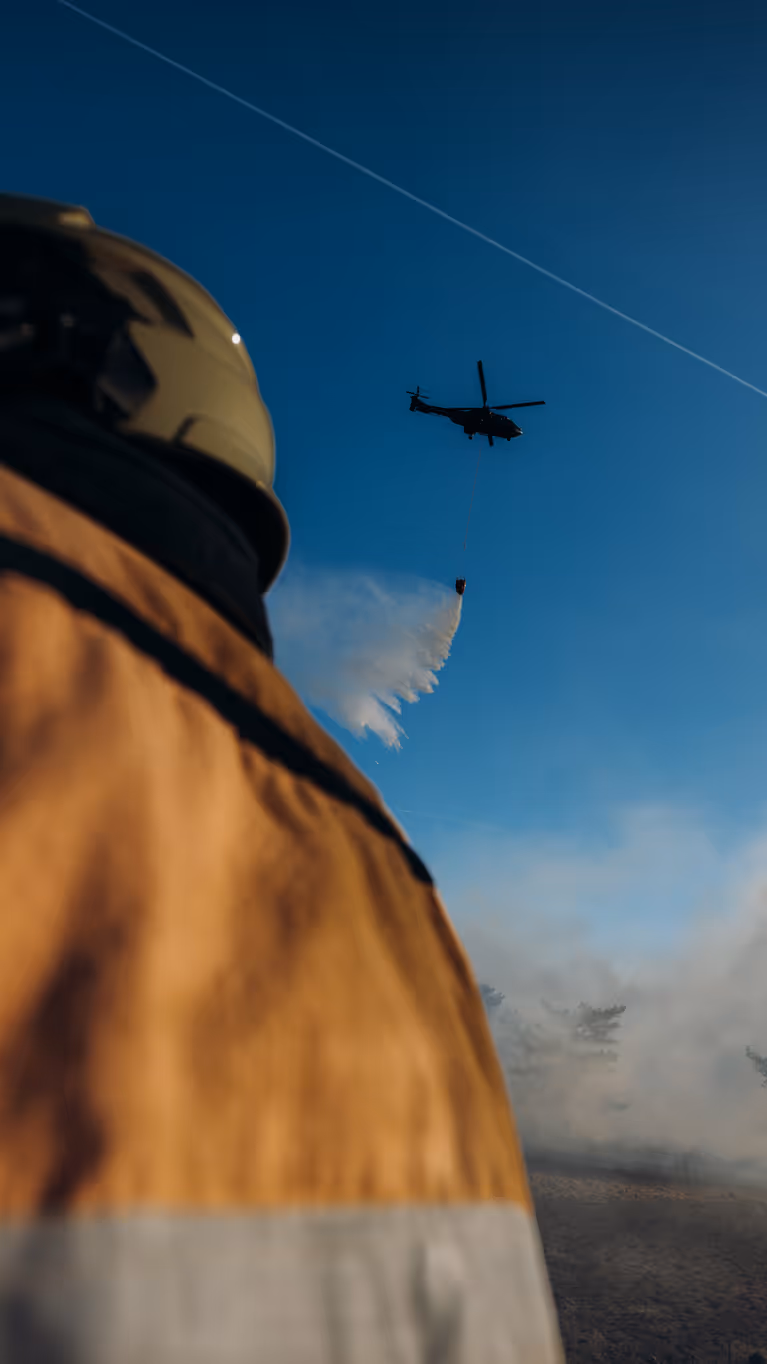Een brandweerman kijkt omhoog en ziet hoe een helikopter bluswater loost op een brandhaard. 