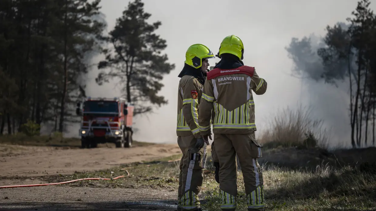 Twee brandweerlieden overleggen in een rookachtig natuurgebied tijdens de bestrijding van een natuurbrand op de Veluwe. 