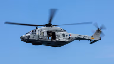 Een draaiende helikopter met bemanningslid in de deuropening. 