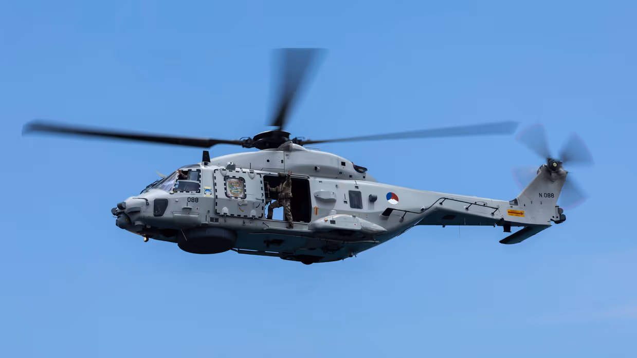 Een draaiende helikopter met bemanningslid in de deuropening. 