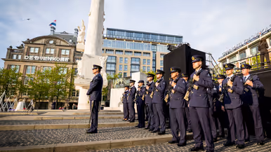 Een detachement luchtmachtmilitairen staat opgesteld naast het Monument op de Dam. In de achtergrond het winkelpand van de Bijenkorf.