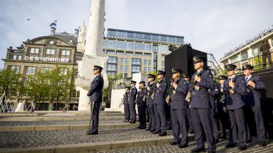 Een detachement luchtmachtmilitairen staat opgesteld naast het Monument op de Dam. In de achtergrond het winkelpand van de Bijenkorf.