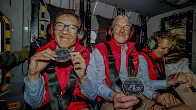 Twee leden van de Jostiband zittend in een NH90 met tonen hun patch ‘Josti Flight; Bevrijdingsdag 2026’.