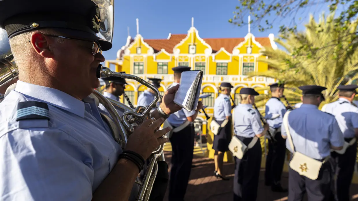 Luchtmachtmuzikanten treden op tegen een achtergrond van gele huizen en palmbomen.