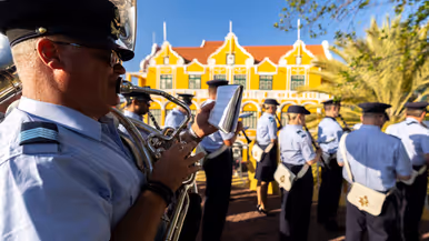 Luchtmachtmuzikanten treden op tegen een achtergrond van gele huizen en palmbomen.