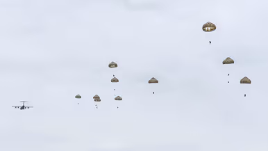 Parachutisten dalen met geopende parachutes neer boven de Belgische heide.