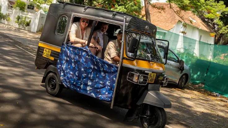 Bemanningsleden zitten lachend in een tuktuk met chauffeur.