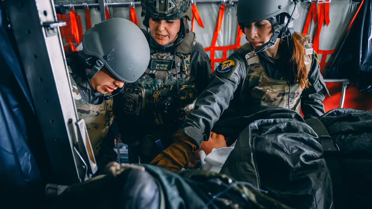 Drie militairen behandelen een patiënt aan boord van een vliegtuig.