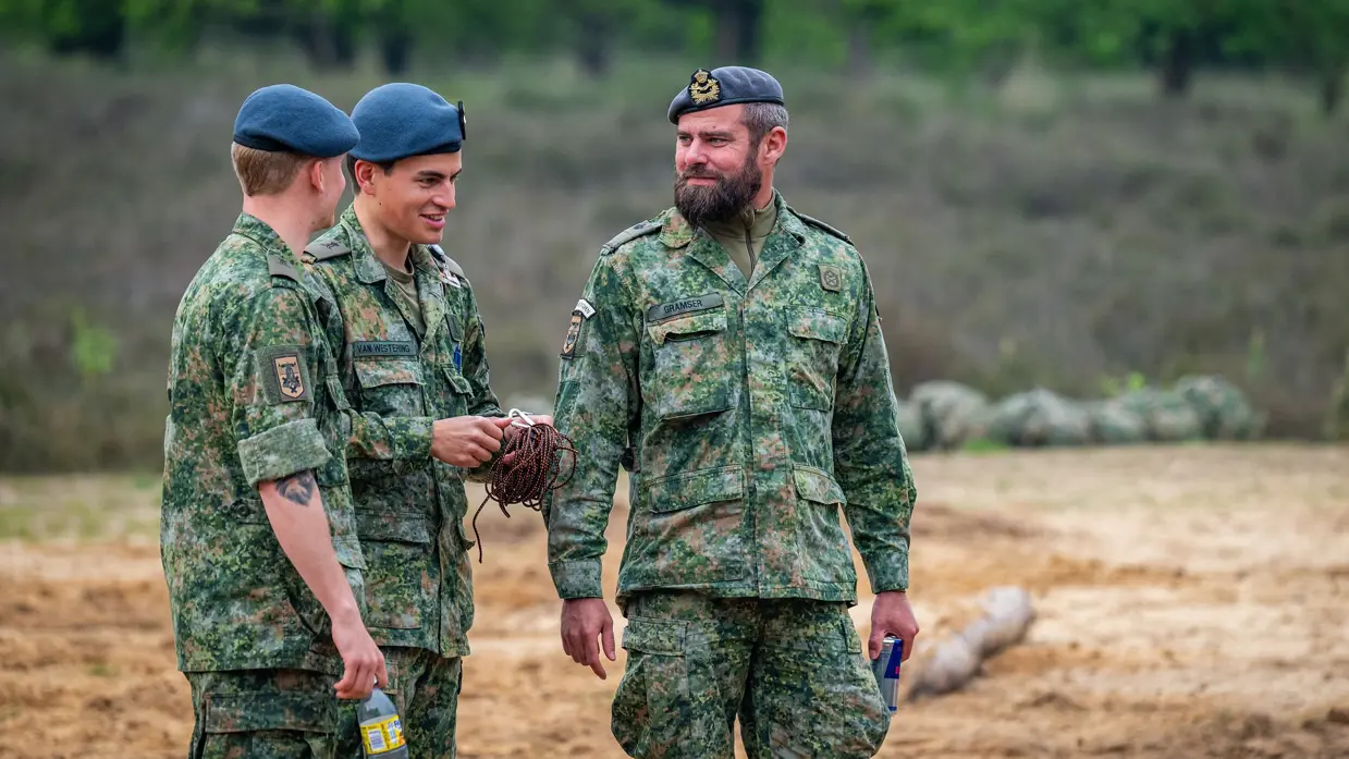 Tim Gramser in actie als instructeur, sprekend met cadetten en portretterend voor de foto, terwijl hij in de camera kijkt en een groen vlekkenpak draagt.  