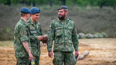 Tim Gramser in actie als instructeur, sprekend met cadetten en portretterend voor de foto, terwijl hij in de camera kijkt en een groen vlekkenpak draagt.  