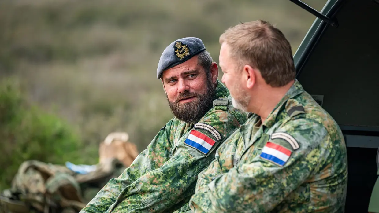 Tim Gramser in actie als instructeur, sprekend met cadetten en portretterend voor de foto, terwijl hij in de camera kijkt en een groen vlekkenpak draagt.  