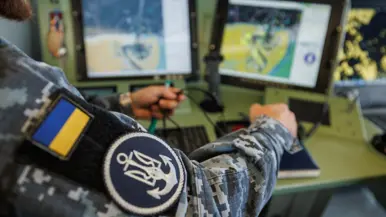 Een militair op de brug, een militair kijkt aan dek door een verrekijker en een militair bedient apparatuur op de brug.