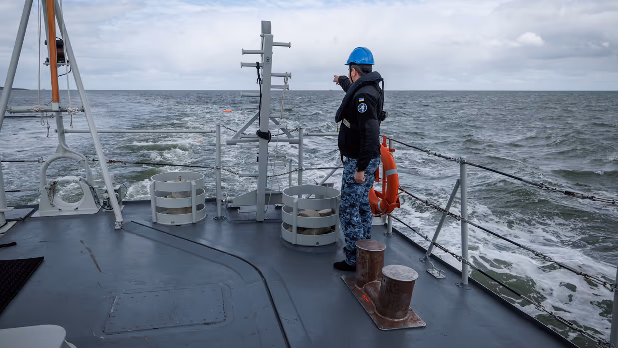 Een militair aan dek wijst naar iets in zee