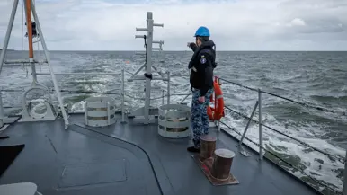 Een militair aan dek wijst naar iets in zee