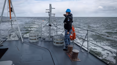 Een militair aan dek wijst naar iets in zee