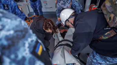 Militairen pakken tijdens de oefening de collega in die drenkeling speelt en warm moet worden gehouden en militairen behandelen deze oefengewonde in het schip.