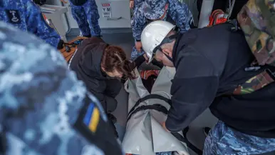 Militairen pakken tijdens de oefening de collega in die drenkeling speelt en warm moet worden gehouden en militairen behandelen deze oefengewonde in het schip.