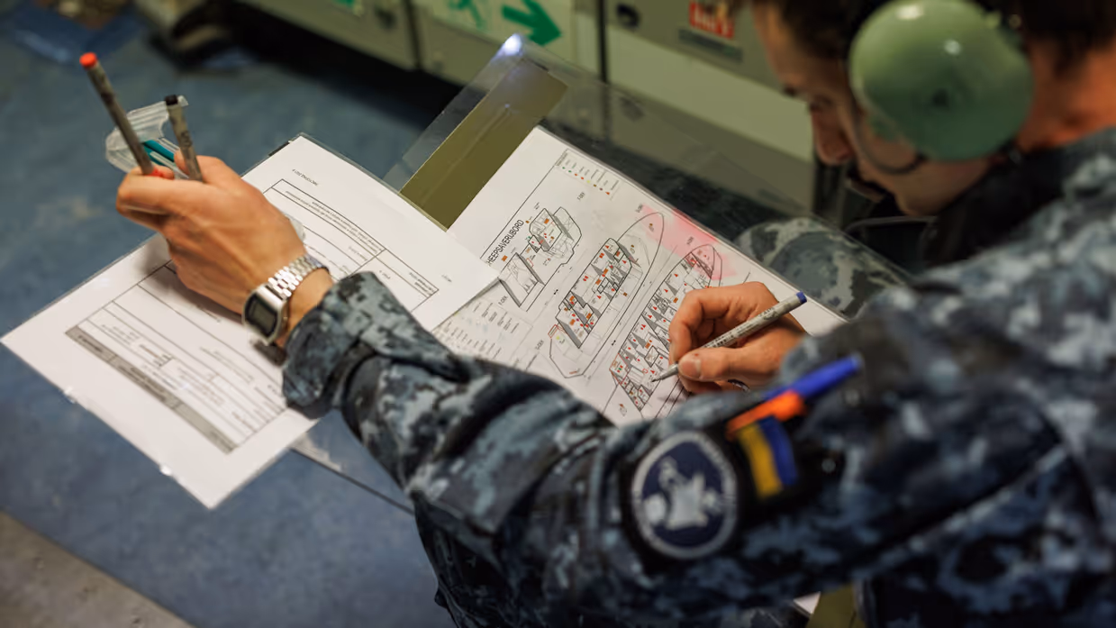 Een militair zit gebogen over plattegronden van het schip