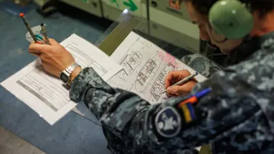 Een militair zit gebogen over plattegronden van het schip