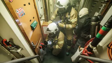 Een opvarende bestrijdt brand in een gang van het schip 