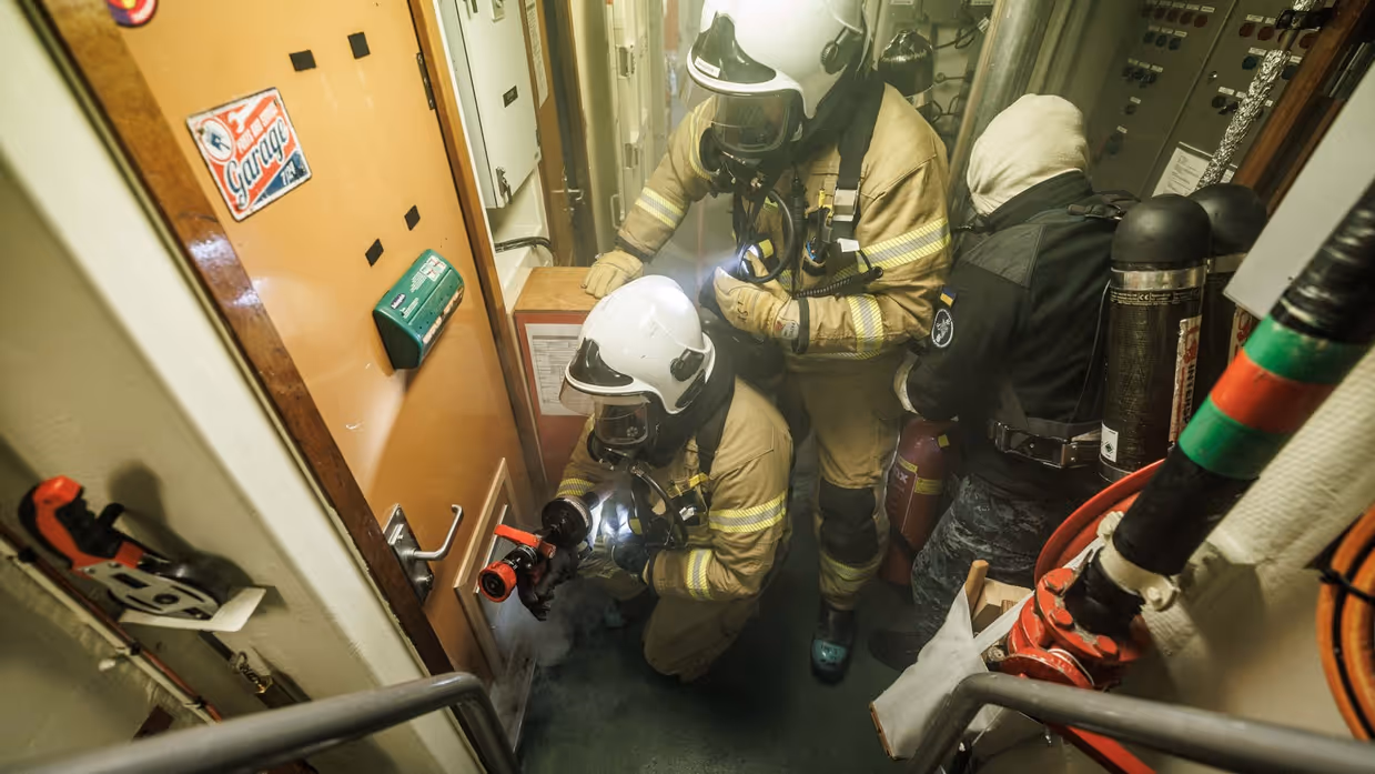 Een opvarende bestrijdt brand in een gang van het schip 