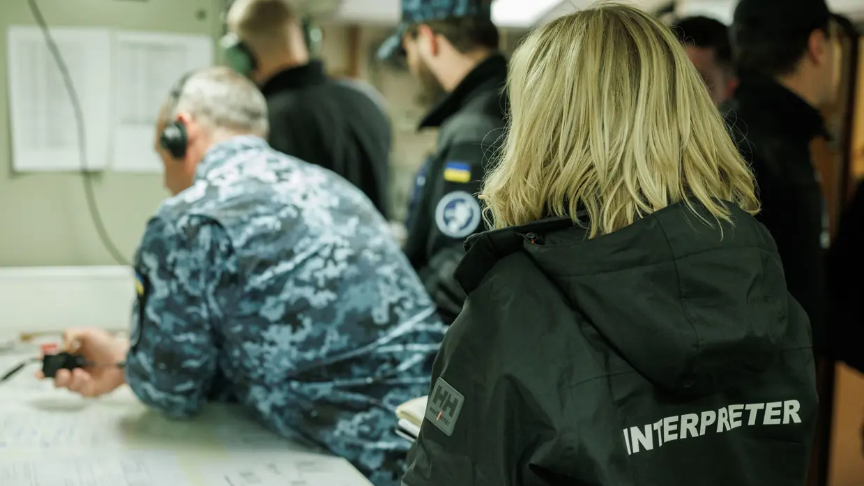 Een tolk met woord ‘interpreter’ op de rug staat achter een groepje militairen.