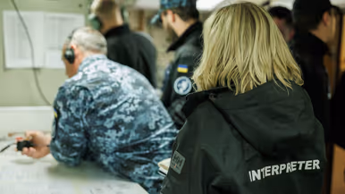 Een tolk met woord ‘interpreter’ op de rug staat achter een groepje militairen.