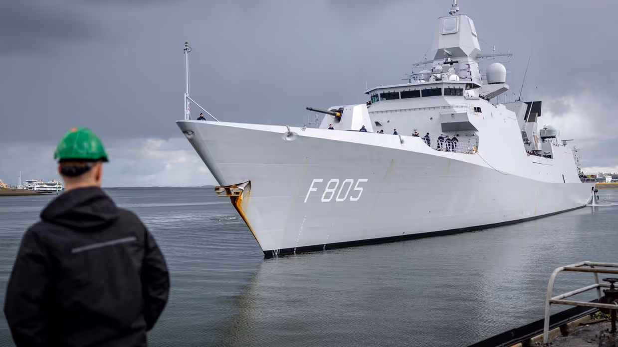 Linkerfoto: twee sleepboten escorteren de Evertsen. Rechterfoto: een marineman hoe de Evertsen richting de kade vaart. 