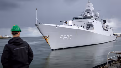Linkerfoto: twee sleepboten escorteren de Evertsen. Rechterfoto: een marineman hoe de Evertsen richting de kade vaart. 