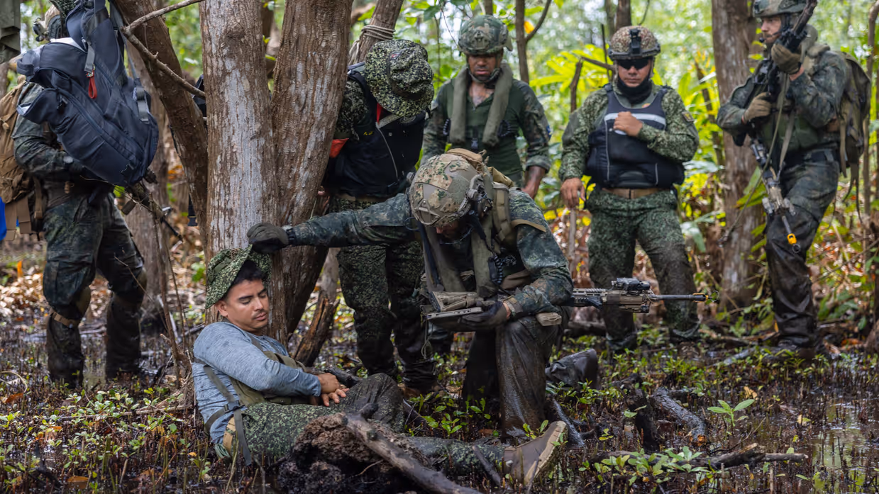 Op de 4 foto’s een Colombiaanse instructeur in een boom, Colombiaanse instructeurs die zogenaamd drugs verstoppen, een Colombiaanse instructeur die een drugslab optuigt en mariniers met een zogenaamd neergeschoten kartelbaas.