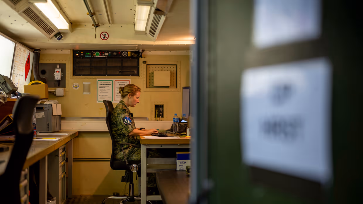 Op de linkerfoto zit Suzanne in haar werkcontainer achter de computer. Op de rechterfoto leunt Suzanne met een arm op een vrachtwagen.